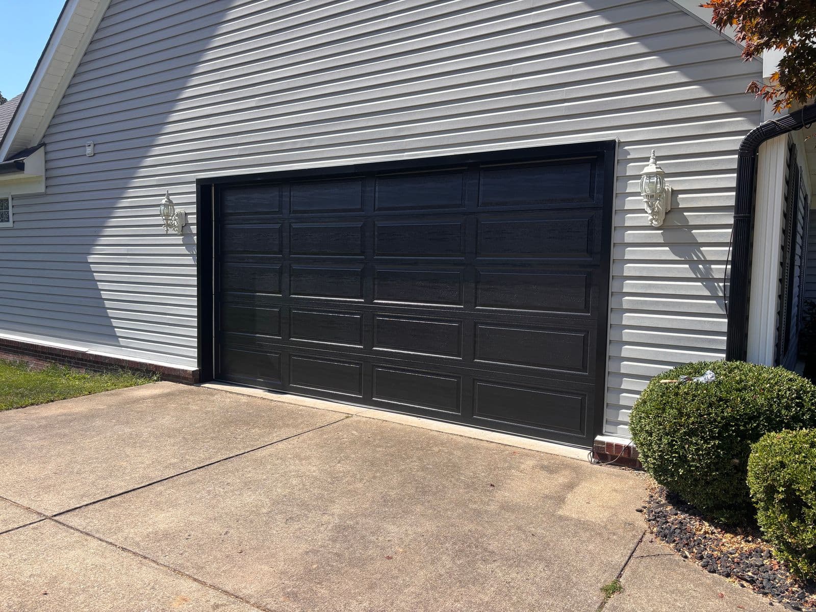 A new black raised-panel garage door on a home with grey siding