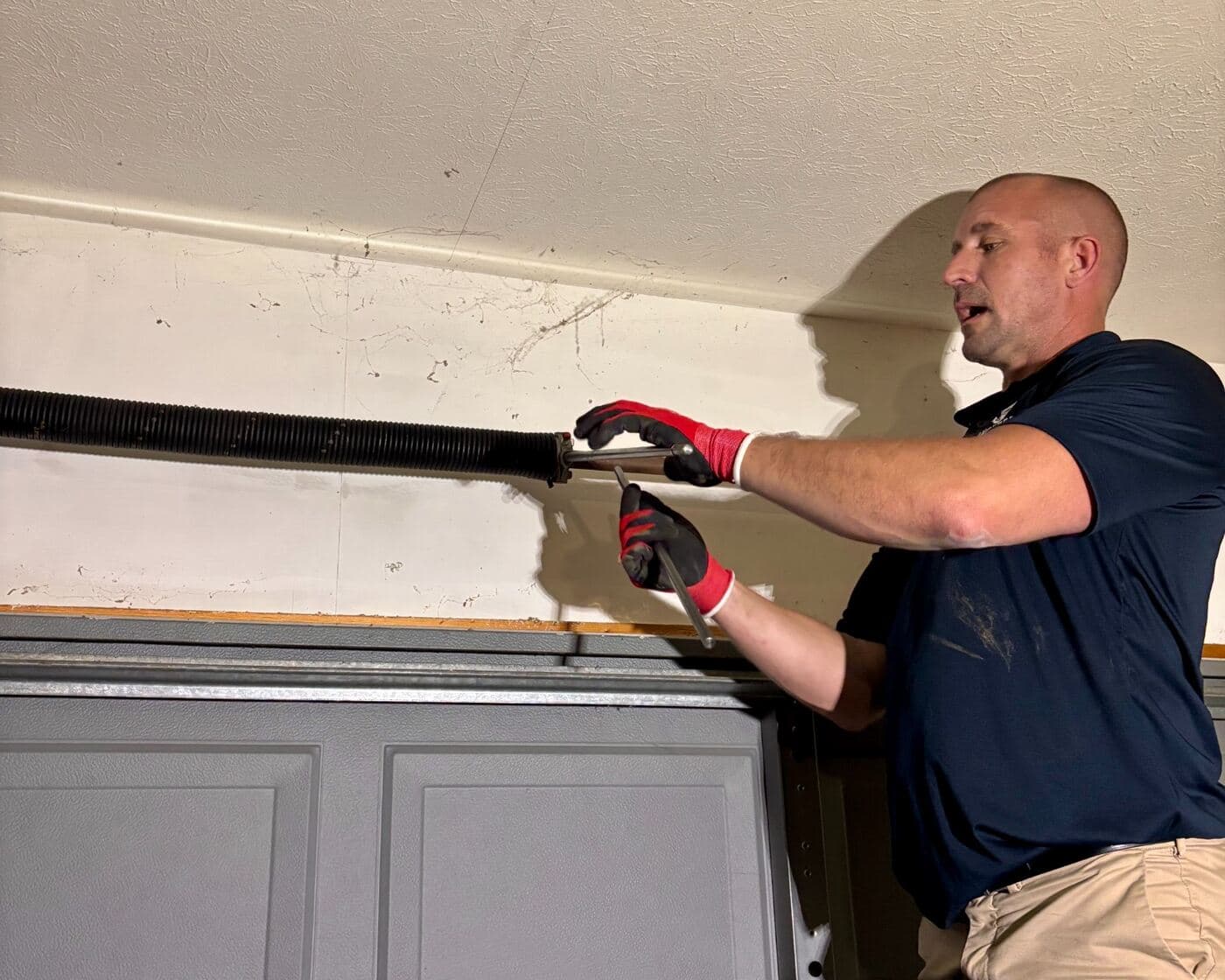 A replacement torsion spring being wound onto the bar above a door.